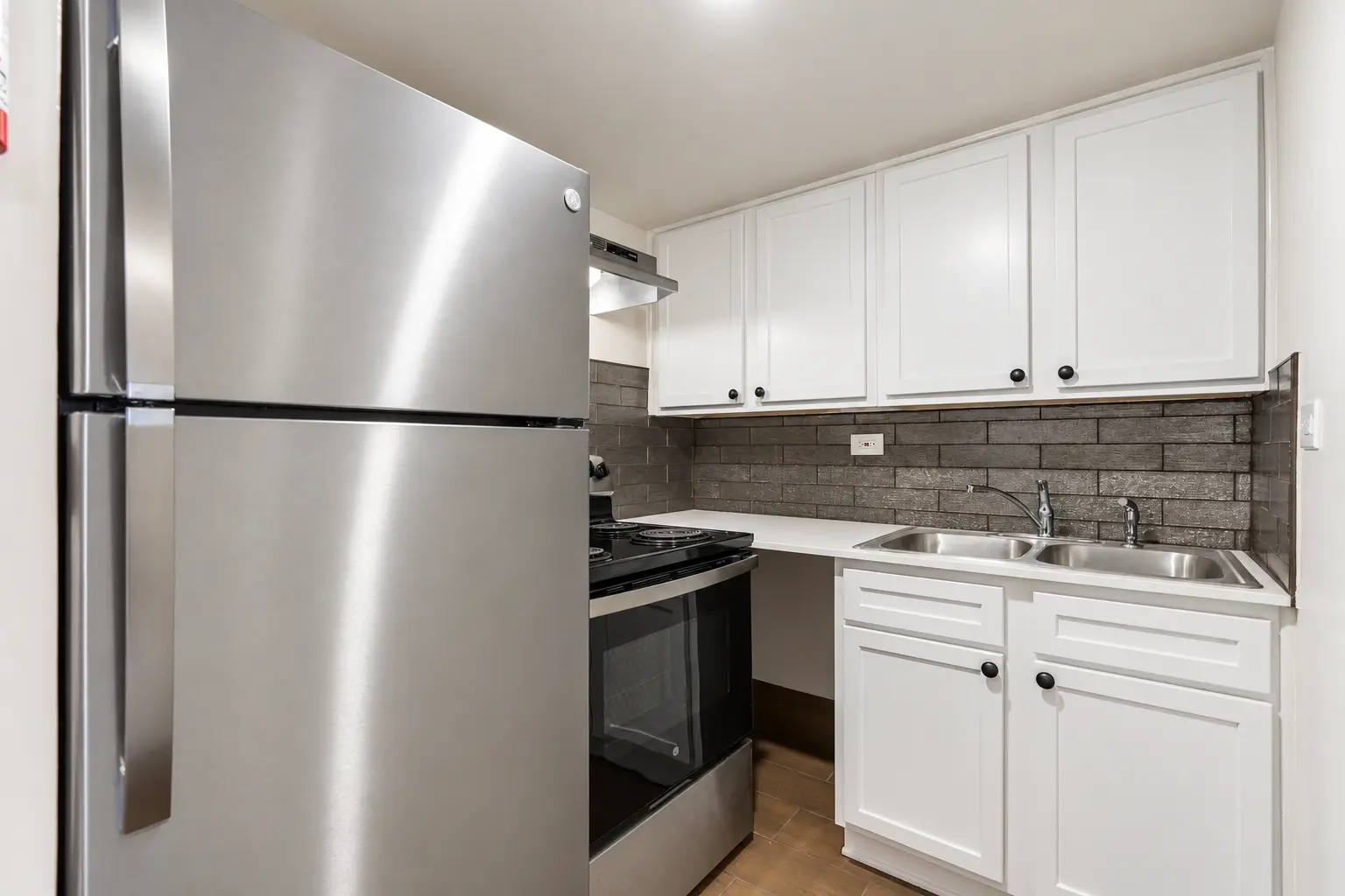 Crescendo kitchen with white cabinetry, dark tile backsplash and stainless steel appliances