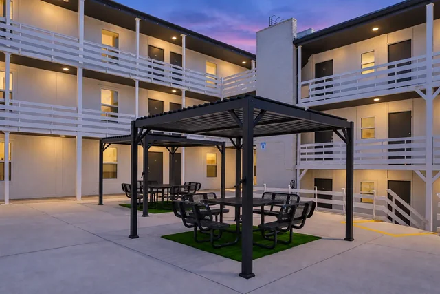 Courtyard with two pergolas and black metal picnic seating between the apartment buildings