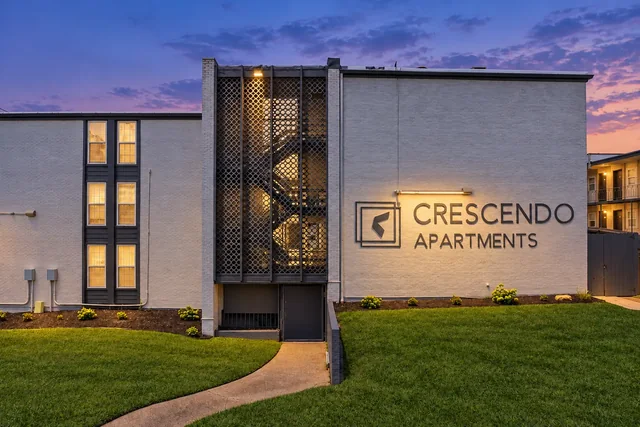 Crescendo Apartments facade with white brick, dark decorative panels, prominent signage, and a green lawn